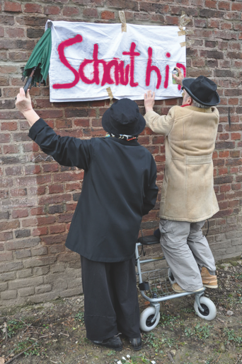 Zwei Senioren hängen ein Plakat mit den Wörtern "Schaut hin" auf.